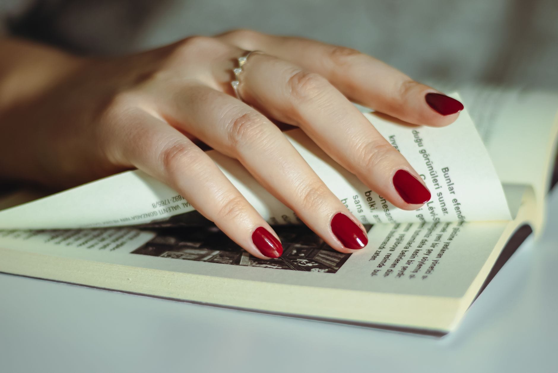 Dłoń z czerwonym manicure przewracająca kartkę książki