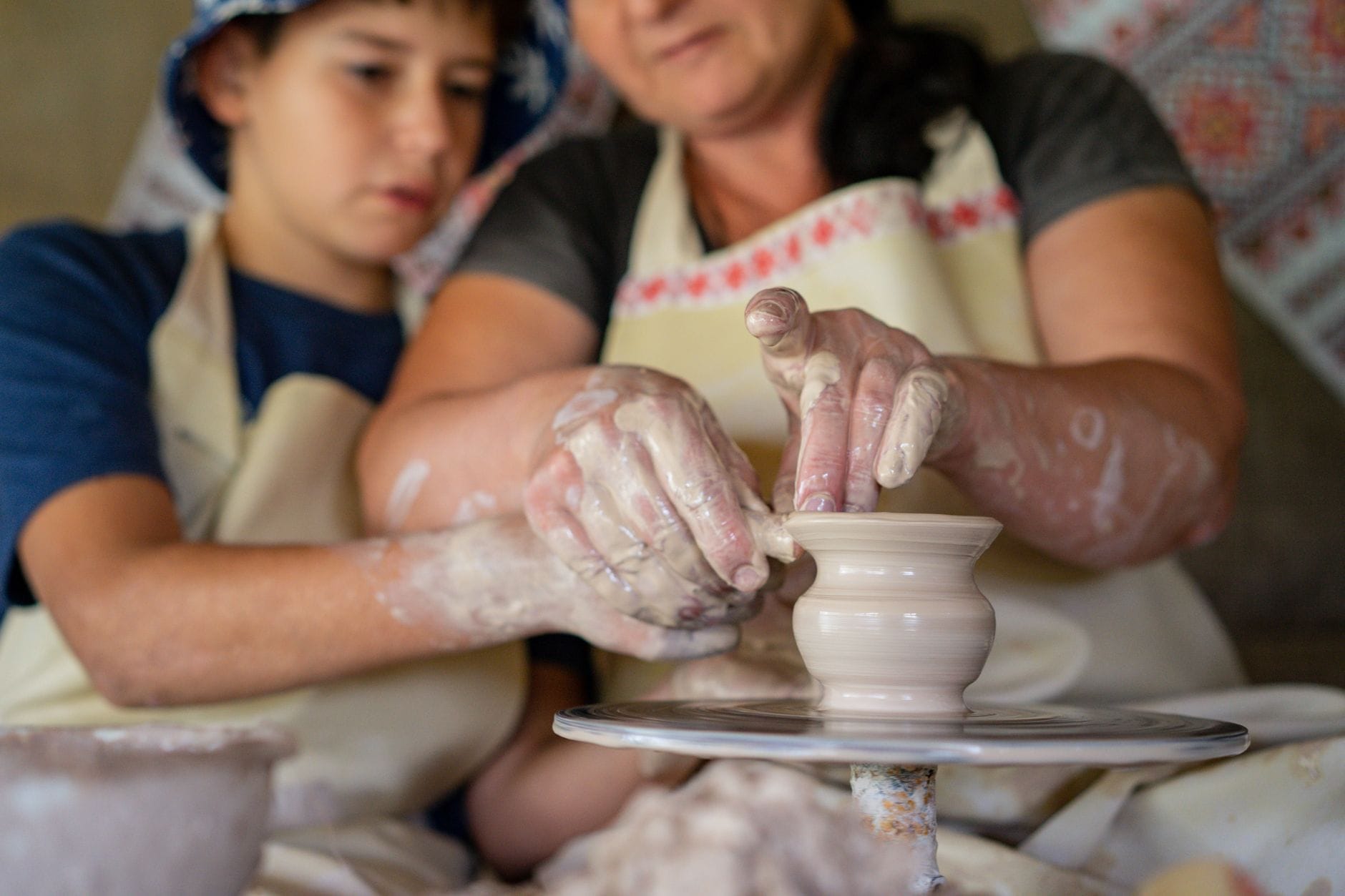 Mama pomaga synowi lepić miskę z gliny na kole garncarskim